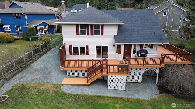 back of house with gravel driveway, roof with shingles, fence, and a wooden deck