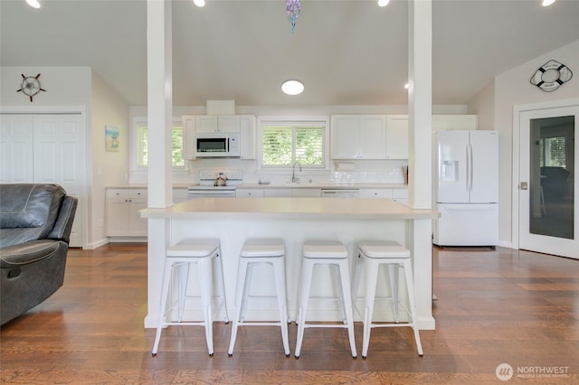 kitchen with light countertops, white appliances, white cabinets, and a kitchen breakfast bar