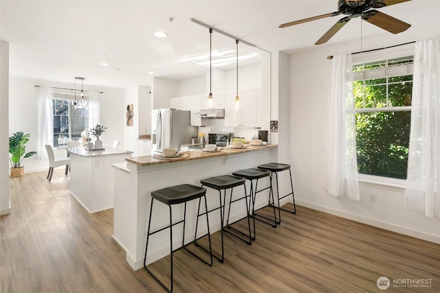 kitchen featuring decorative light fixtures, white cabinetry, a peninsula, under cabinet range hood, and stainless steel fridge with ice dispenser