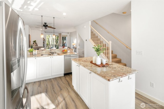 kitchen with stainless steel appliances, a sink, a kitchen island, white cabinets, and light stone countertops