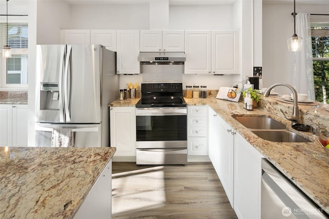 kitchen with hanging light fixtures, stainless steel appliances, under cabinet range hood, white cabinetry, and a sink