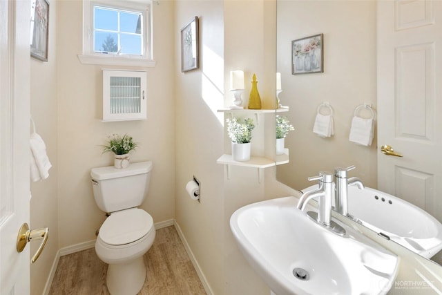 half bath with wood finished floors, a sink, toilet, and baseboards