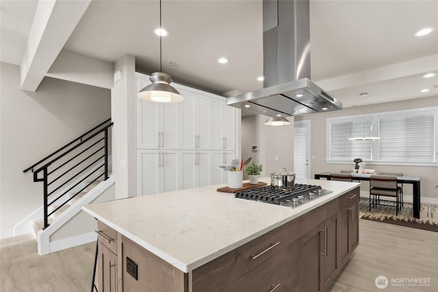 kitchen featuring decorative light fixtures, stainless steel gas stovetop, light wood-style flooring, a kitchen island, and island range hood