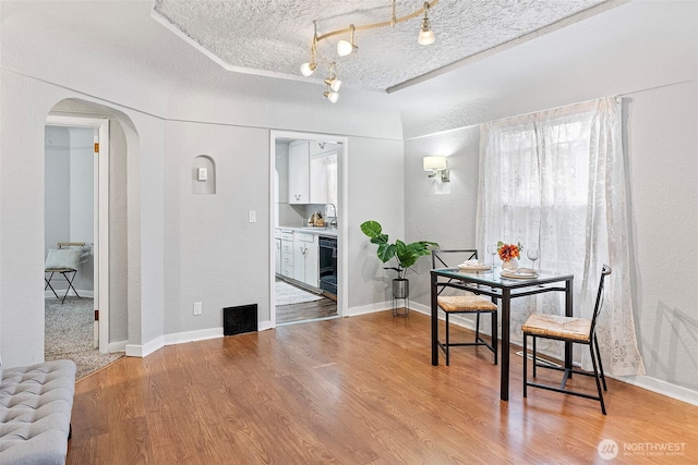 dining space featuring arched walkways, a textured ceiling, wood finished floors, baseboards, and a tray ceiling