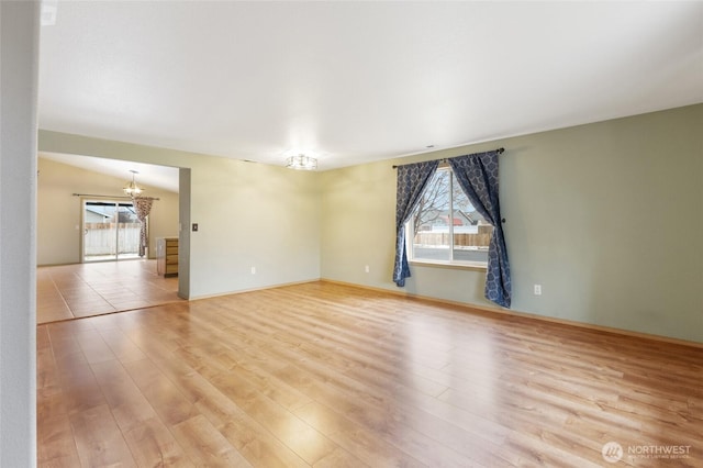 empty room featuring a chandelier, baseboards, and light wood-style floors