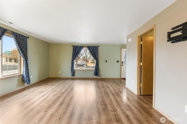 empty room with light wood finished floors, visible vents, and baseboards