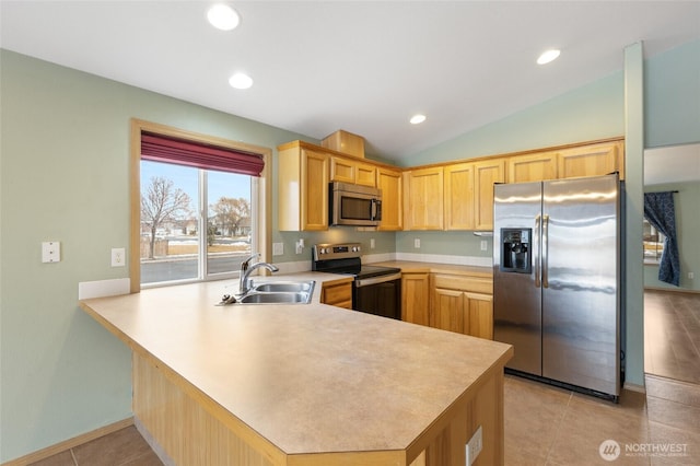 kitchen with a peninsula, a sink, vaulted ceiling, light countertops, and appliances with stainless steel finishes