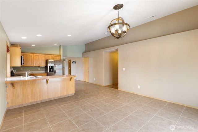 kitchen with a breakfast bar area, a peninsula, light countertops, light brown cabinetry, and stainless steel fridge