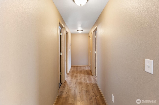 corridor featuring light wood-type flooring and baseboards