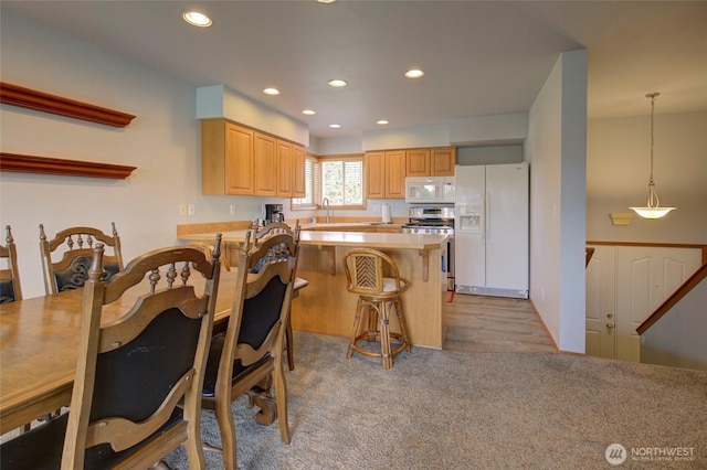 kitchen featuring a breakfast bar, recessed lighting, light countertops, a sink, and white appliances