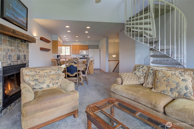 living area with a tile fireplace, light colored carpet, stairway, and recessed lighting