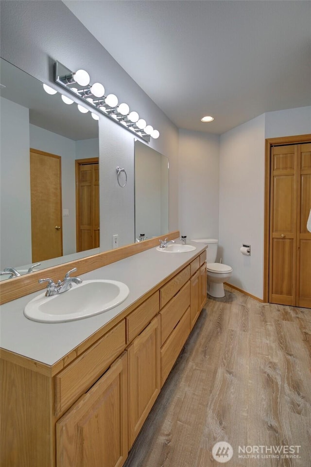 full bath featuring double vanity, a sink, toilet, and wood finished floors