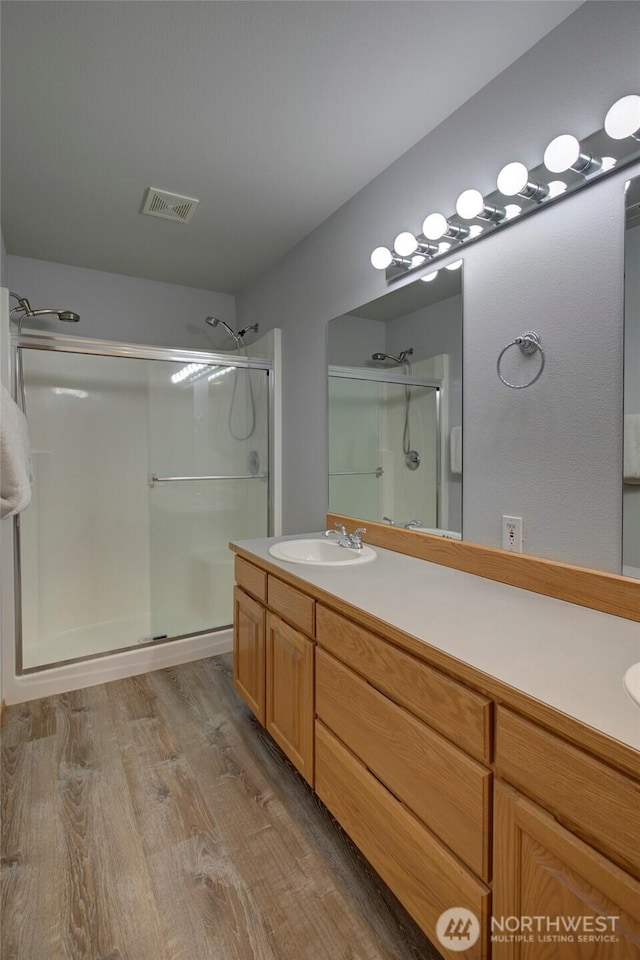 bathroom with a stall shower, visible vents, vanity, and wood finished floors