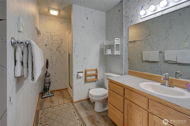 full bathroom with wallpapered walls, toilet, wood finished floors, vanity, and a shower stall