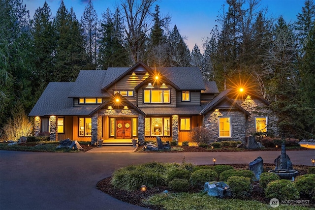 back of property at dusk featuring stone siding and driveway