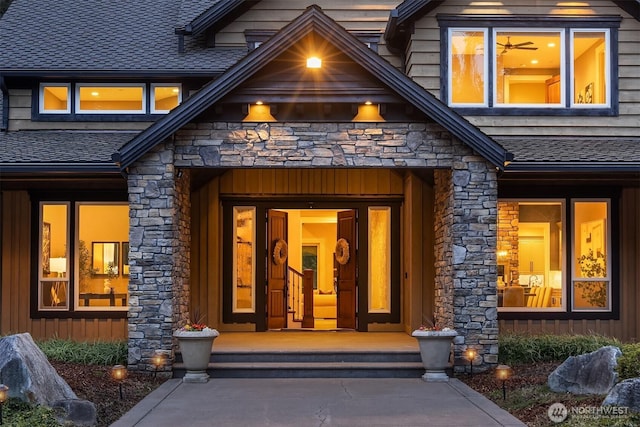 entrance to property featuring stone siding, a shingled roof, and board and batten siding