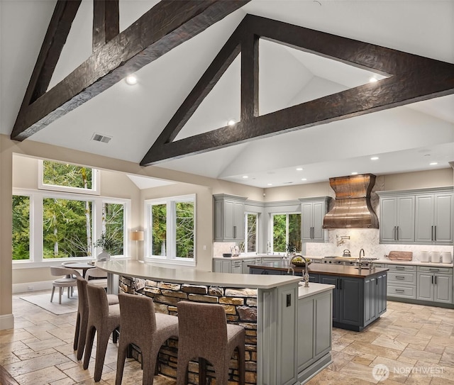 kitchen featuring custom range hood, a kitchen island with sink, gray cabinets, and stone tile flooring