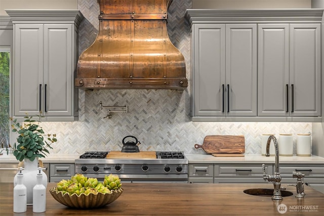 kitchen featuring tasteful backsplash, gray cabinets, custom range hood, a sink, and range