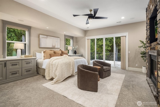 bedroom with access to exterior, multiple windows, light colored carpet, and a stone fireplace