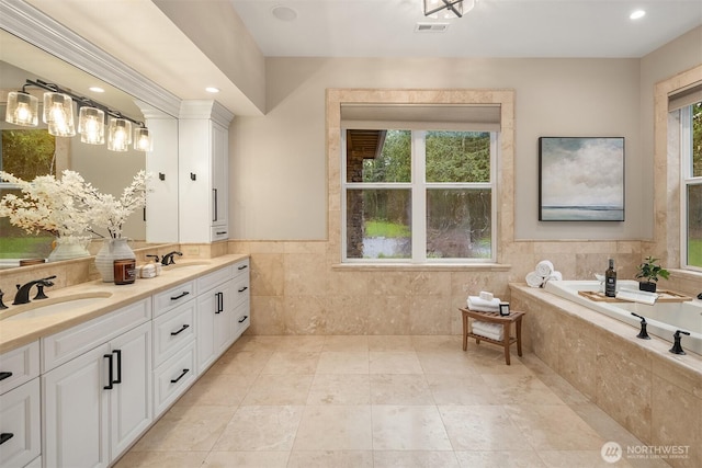 full bath with a sink, visible vents, tile walls, a bath, and double vanity