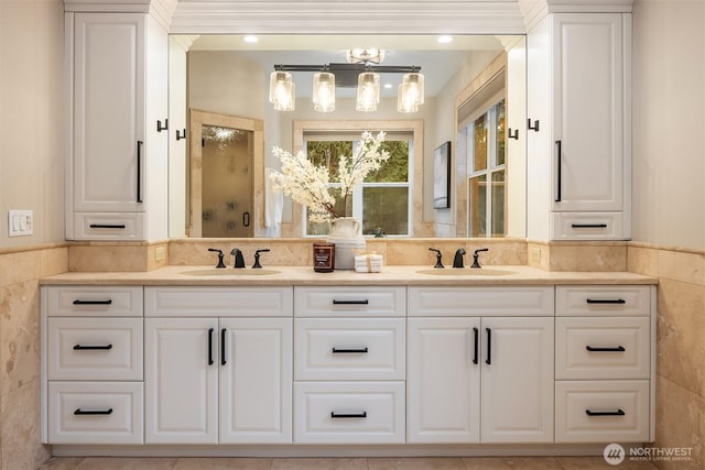 full bathroom with double vanity, a sink, a shower with door, and tile walls