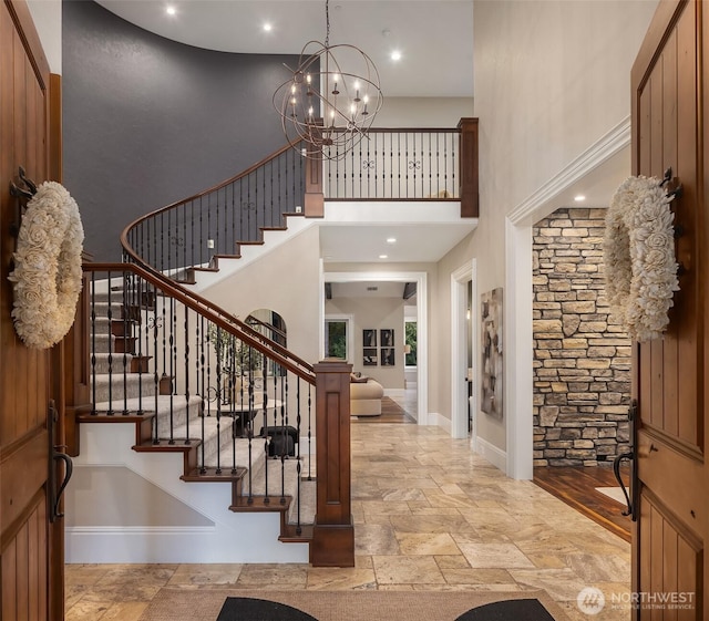 foyer with baseboards, an inviting chandelier, a towering ceiling, and stone tile floors