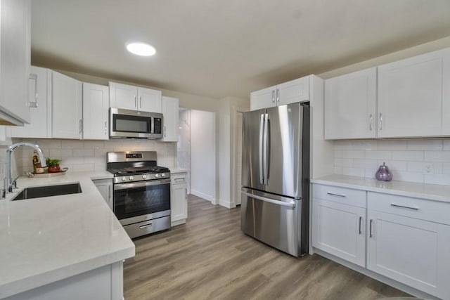 kitchen featuring light wood finished floors, white cabinets, stainless steel appliances, light countertops, and a sink