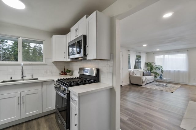 kitchen with stainless steel appliances, light countertops, open floor plan, white cabinets, and a sink