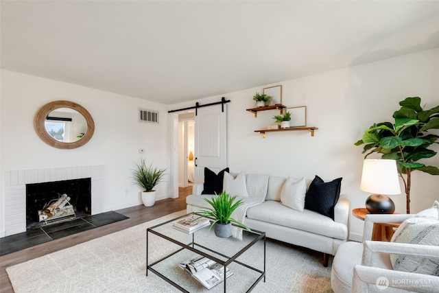 living room with a barn door, a fireplace, visible vents, baseboards, and dark wood-style floors