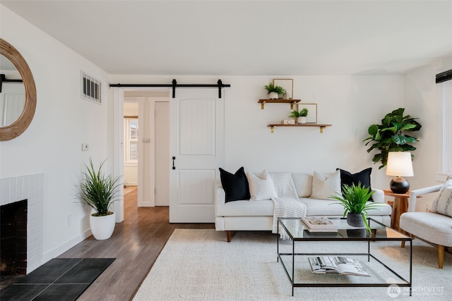 living room featuring dark wood-style flooring, a fireplace, visible vents, a barn door, and baseboards