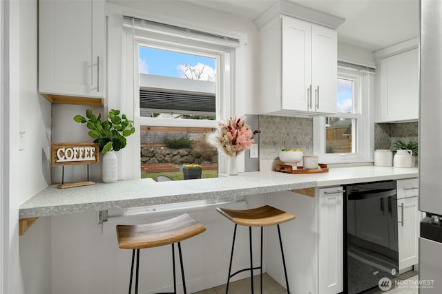 kitchen with a healthy amount of sunlight, white cabinets, backsplash, and a kitchen breakfast bar