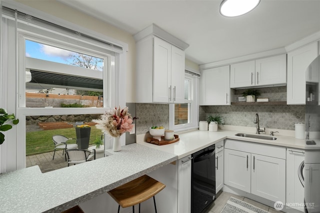 kitchen featuring black dishwasher, light countertops, white cabinetry, a sink, and plenty of natural light