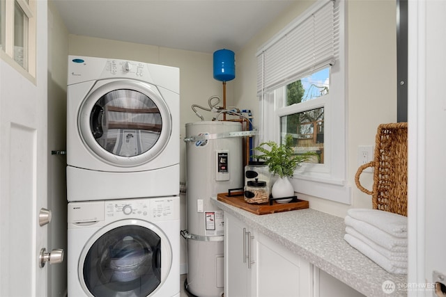 washroom featuring water heater, laundry area, and stacked washer / drying machine