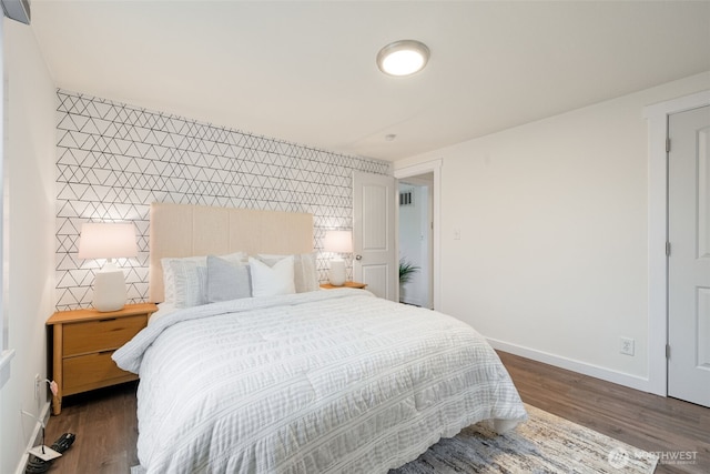 bedroom featuring an accent wall, dark wood-style flooring, and baseboards