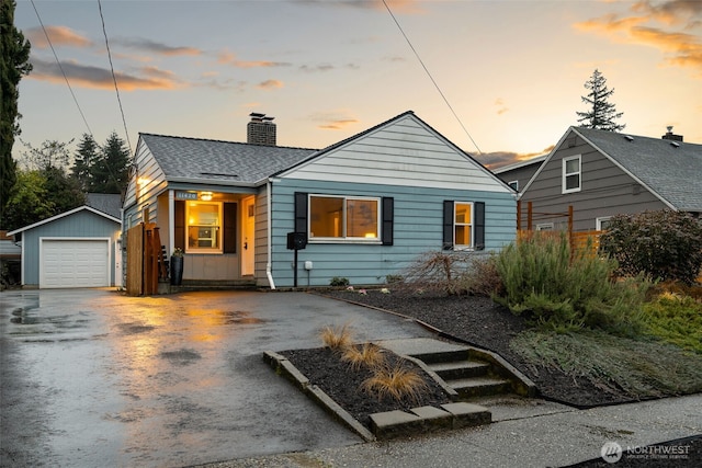 bungalow-style home featuring aphalt driveway, an outbuilding, a chimney, a shingled roof, and a garage