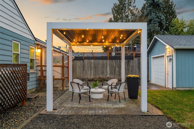 patio terrace at dusk featuring an outbuilding, a fenced backyard, and a detached garage