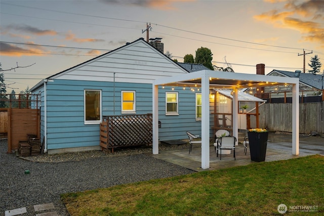 back of property at dusk featuring a patio area, fence, and a lawn