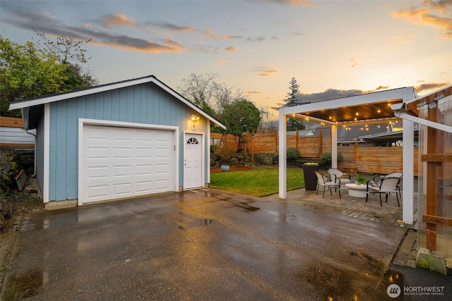 garage at dusk featuring a garage, driveway, and fence