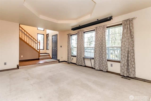 spare room featuring a tray ceiling, light colored carpet, visible vents, baseboards, and stairs