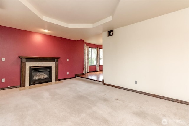 unfurnished living room featuring baseboards, a raised ceiling, a tile fireplace, and light colored carpet