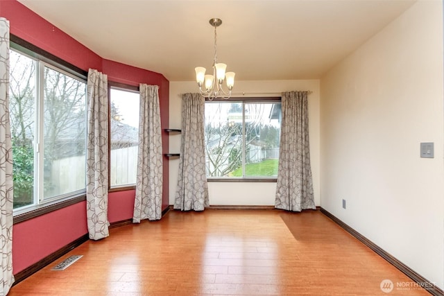 unfurnished dining area featuring baseboards, visible vents, a chandelier, and wood finished floors