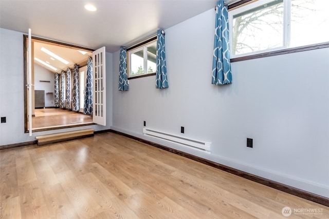 spare room featuring a baseboard heating unit, vaulted ceiling, baseboards, and wood finished floors