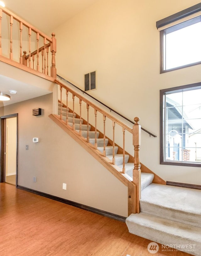 stairway featuring plenty of natural light, wood finished floors, a towering ceiling, and baseboards