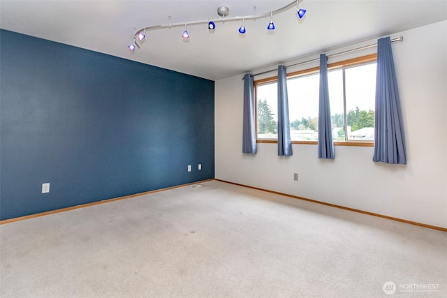 spare room featuring carpet flooring, rail lighting, and baseboards