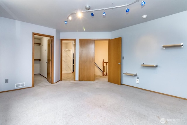 unfurnished bedroom featuring ensuite bathroom, light colored carpet, visible vents, baseboards, and track lighting