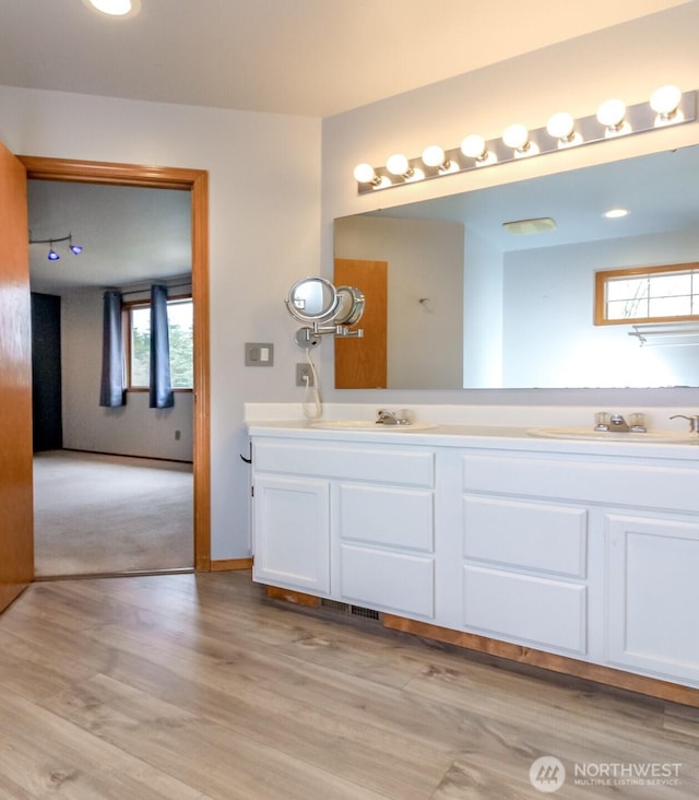 full bathroom with wood finished floors, a sink, baseboards, and double vanity