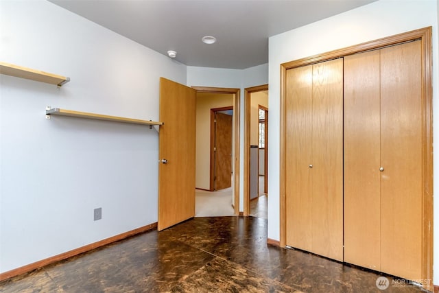 unfurnished bedroom with concrete floors, baseboards, and a closet