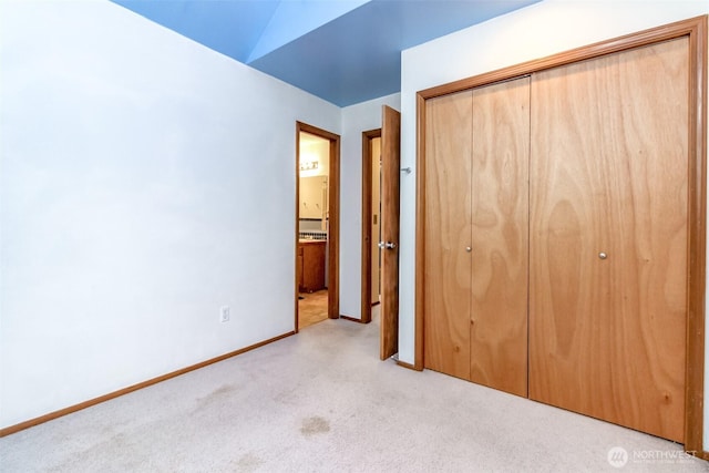 unfurnished bedroom featuring baseboards, vaulted ceiling, a closet, and light colored carpet