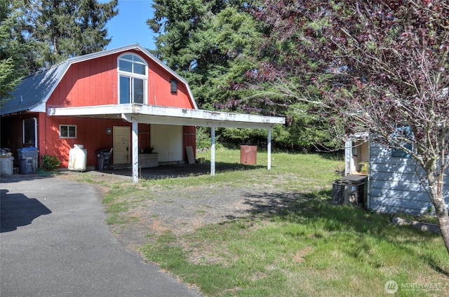 view of side of home with a yard, central air condition unit, a gambrel roof, a carport, and driveway