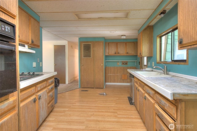 kitchen with a sink, visible vents, light wood-type flooring, tile counters, and dishwasher